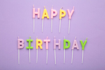 Colorful candles in letters saying Happy Birthday on purple background