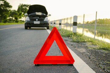 Close-up of a red emergency stop sign on a background of a broken black car on the road. Red emergency stop sign with broken down car on the road waiting to be repaired.