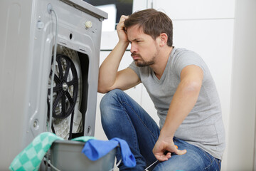 upset young man sitting next to washing machine