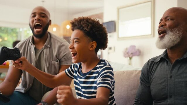 Multi-generation male family sitting on sofa at home holding controllers playing video game together giving each other high five  - shot in slow motion
