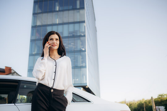 Attractive young businesswoman in white suit talking phone standing near business centre