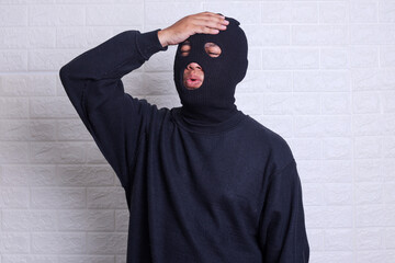 man wearing burglar mask and black shirt surprised with hand on head for mistake forgot something