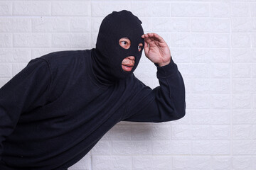 A criminal wearing black balaclavausing torch and spying isolated on white studio background