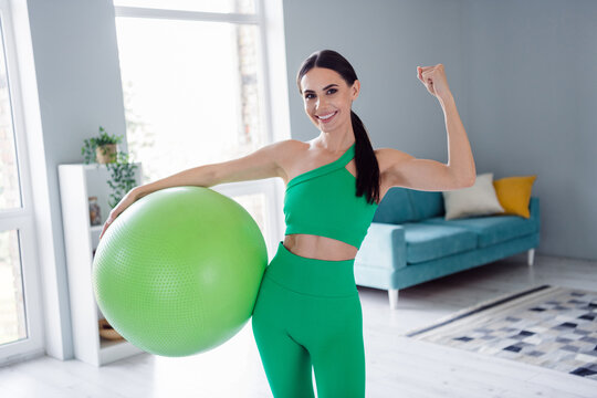 Photo of confident cool lady wear sporty outfit rising fist showing arm muscles holding fit ball indoors home studio