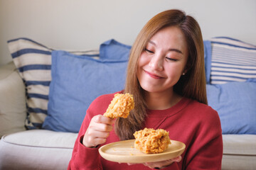 Portrait image of a young woman holding and eating fried chicken at home