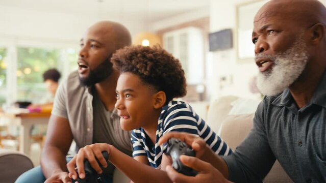 Multi-generation male family sitting on sofa at home holding controllers playing video game together giving each other high five  - shot in slow motion