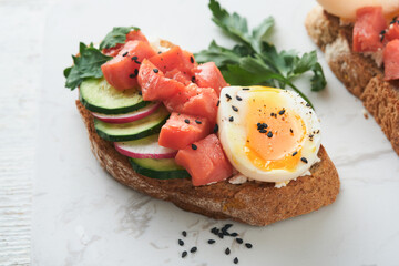 Healthy sandwich with bread or toast, smoked salmon, soft egg, cream cheese, cucumber, radish, black sesame and parsley on old wooden table. Delicious protein fish sandwich for breakfast. Smorrebrod.