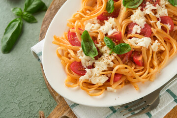 Salad caprese or pasta spaghetti broken with basil and mozzarella ala caprese on white plate on green rustic wooden background. Traditional Italian cuisine. Italian food concept. Top view. Recipe.