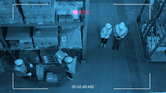 Top view security camera shot of four workers in uniforms and hard hats working in warehouse
