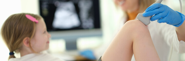 Doctor pediatrician conducting ultrasound examination of knee joint of child in clinic closeup....