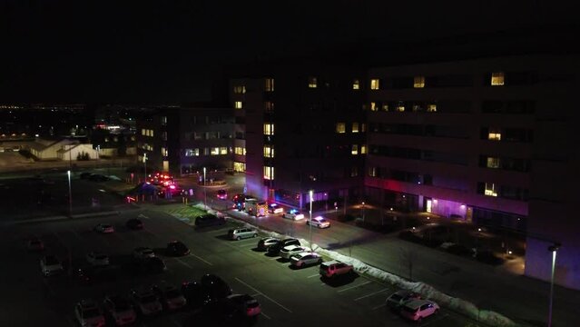 Emergency Medical service vehicles police and fire trucks outside apartment building at night