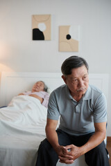 Pensive worried senior man sitting on bed of his sick wife