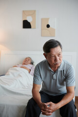 Obraz premium Pensive worried senior man sitting on bed of his sick wife