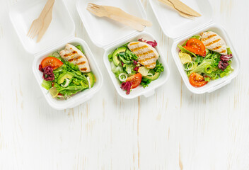 Lunch boxes with salad and grilled chicken on white wooden background. Top view