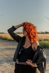A beautiful young woman in a black leather jacket stands in a field near windmills