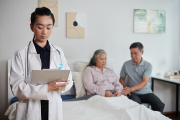 Obraz premium Serious doctor filling medical document after talking to sick senior woman and her husband