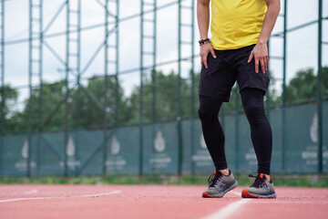 Fototapeta na wymiar Sportsman in leggings and shorts training on running track with rubber surface and white lines on urban sports arena jogger exercising at stadium closeup