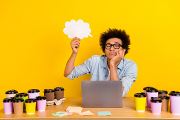 Portrait of unsatisfied guy arm hold empty space cloud shape card desk workplace coffee cup netbook isolated on yellow color background