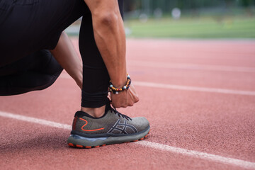Fototapeta na wymiar Man tying sneaker laces squatting on rubberized running track taking break in training on urban ground athlete in sports shoes exercising at outdoor arena closeup