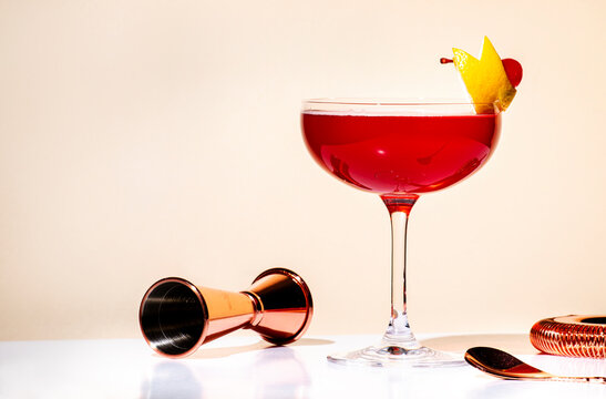 New Yorker red cocktail with whiskey, grenadine, bitter, lemon and ice garnished with lemon zest and cocktail cherry in glass. Beige background, hard light