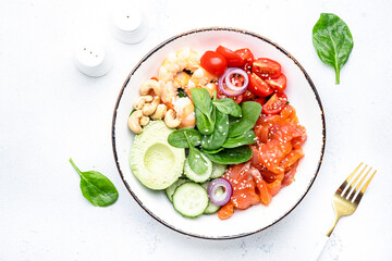 Keto salad with spinach, salmon, shrimp, avocado, cucumber, tomato, nuts, sesame seeds. Low-carbohydrate lunch rich in healthy fats. White table background, top view