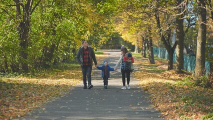 Fototapeta premium A happy young family walks along a city park road in the fall.