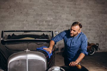 a middle-aged man wipes down a retro car in his garage