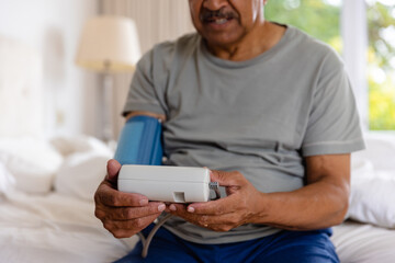 Mid section of biracial senior man taking blood pressure in bed at home - Powered by Adobe