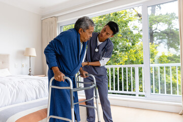 Fototapeta na wymiar Diverse male doctor helping senior male patient using crutches at home