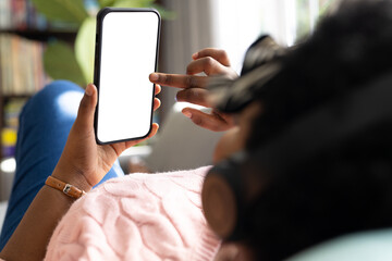 Plus size african american woman with headphones using smartphone with copy space on screen at home