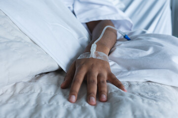 Obraz na płótnie Canvas Close up of hand of african american female patient with drip on hand, lying on bed in hospital room