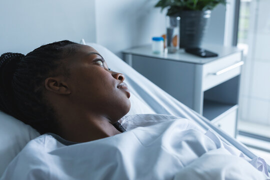 African american female patient looking away, lying on bed in hospital room