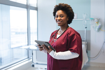 Portrait of happy african american female doctor wearing scrubs and stethoscope, holding tablet