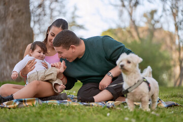 young couple having a picnic sitting on the grass playing with their baby lovingly