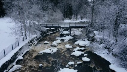 Drone view over a river and a bridge in the middle of a forest during a snowy winter