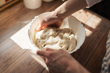 Girl knead dough for baking bread in a plate. Sunny morning in the kitchen, girl hostess baking...