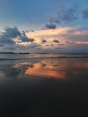 the sky reflected in water on a beach at sunset with clouds and trees