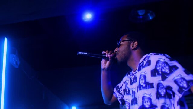 Black african male man artist singer rapper showman performs  performs concert party on the club stage in dark scenery with neon lights blue theme