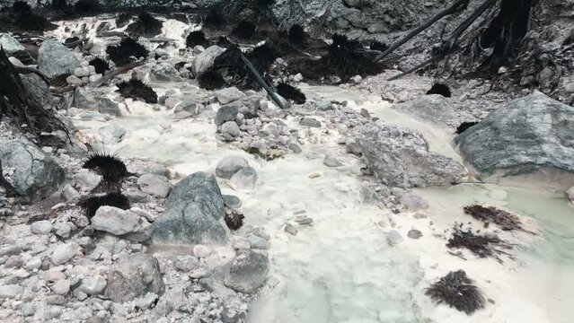 Drone flyng low level on frozen stream following on white rocky ground in the forest
