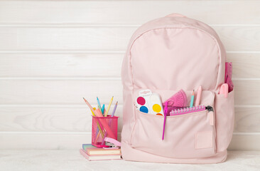 Pink school backpack with stationery on wooden table