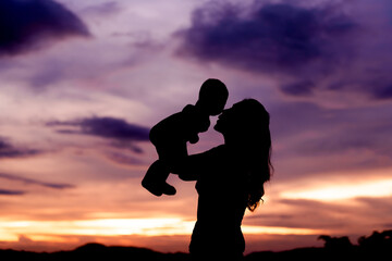 silhouette of mother holding and kissing with infant baby at sunset