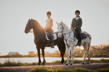 Horse riding, sunset and hobby with friends in nature on horseback by the lake during a summer...