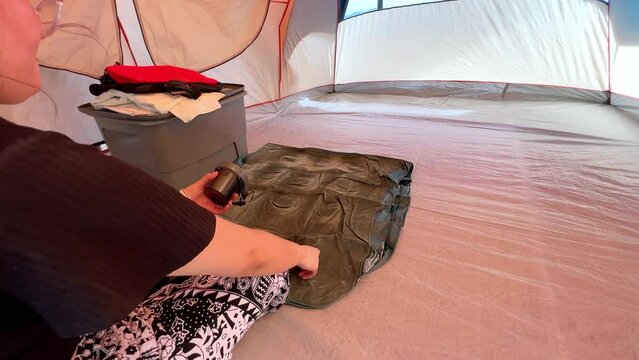 Woman inflating air mattress inside camping house at campground.  