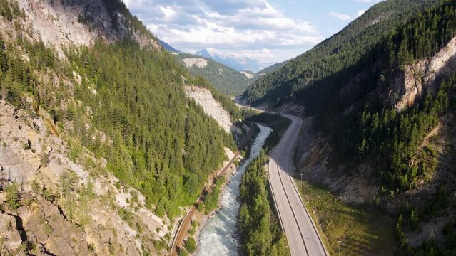 British Columbia Aerial view. Drone flying over the highway surrounded by dense green pine woods revealing mountains in background, British Columbia, Canada. 4K drone footage
