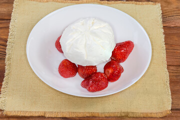 Ice cream piece atop fresh strawberry on the white dish