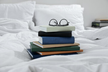 Hardcover books and glasses on bed indoors