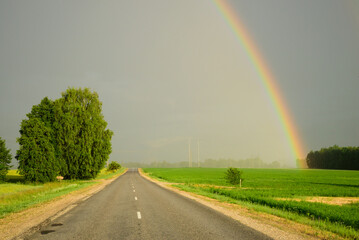 a rainbow sweeps across an asphalt road on a sunny day with rain approaching