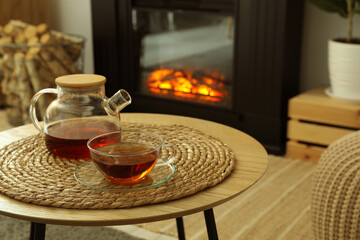 Teapot and cup of drink on coffee table near stylish fireplace in cosy living room. Interior design