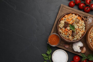 Delicious pilaf and products on black table, flat lay. Space for text