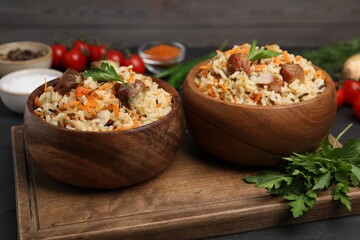 Delicious pilaf with meat and carrot in bowls on black table, closeup